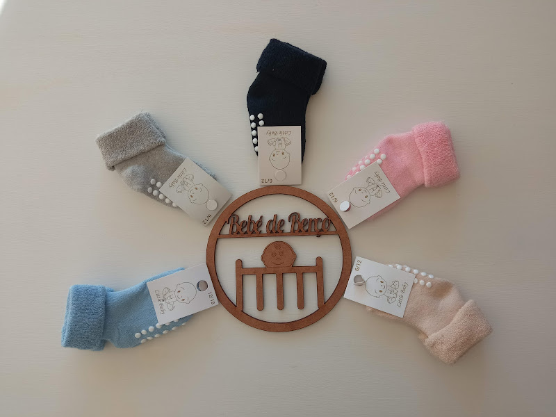 Cinco pares de meias antiderrapantes para bebé em várias cores em volta de um círculo de madeira com texto