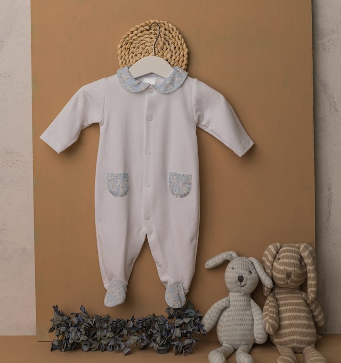 Macacão de bebé branco com detalhes azuis e dois brinquedos de peluche ao lado