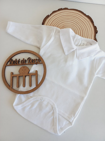 Body branco para bebé com gola e fechos de pressão, sobre base que imita madeira e placa de madeira decorativa.