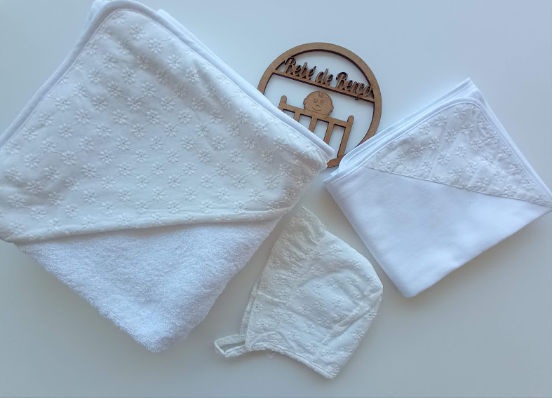 Três toalhas brancas com detalhes em relevo e uma placa de madeira redonda com texto e ícones gravados.