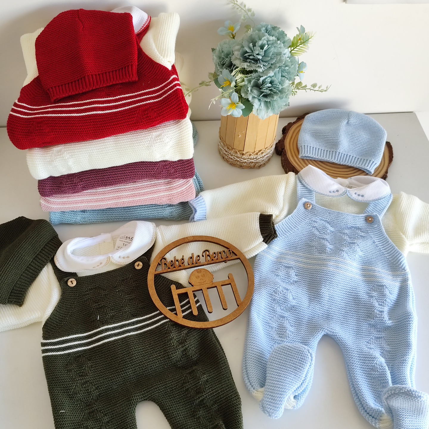 Conjunto de macacão de malha para bebé em azul e verde com camisolas e toucas, flores artificiais ao lado