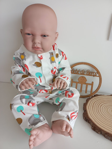 Boneco de bebé com pijama branco estampado colorido sentado com ornamento de madeira