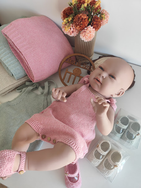 Boneca com fato e sapatos cor-de-rosa de malha junto a mantas e flores