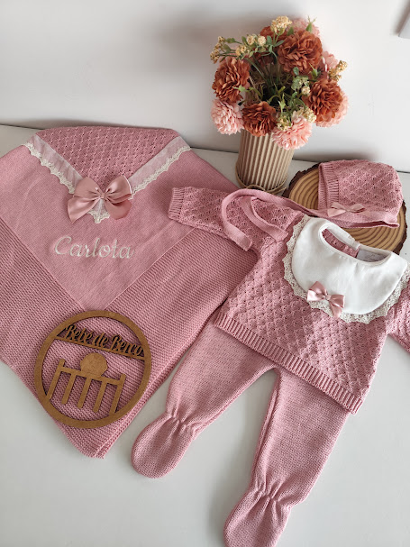 Conjunto de roupa de bebé rosa em malha com manta bordada, macacão, babete e chapéu, com vaso de flores