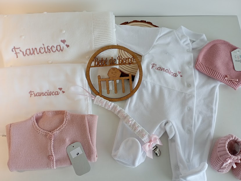 Conjunto de roupa de bebé branca e rosa com bordados e suporte redondo em madeira