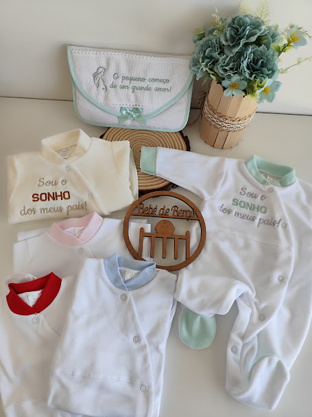 Conjunto de roupa de bebé branca com detalhes coloridos, bordados com frases, fralda bordada, vaso de flores artificiais e ornamento de madeira