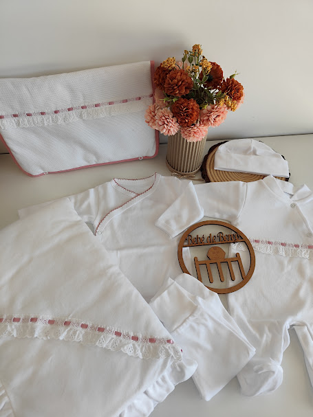 Conjunto de roupa de bebé branco com bordados rosa e flores secas em vaso