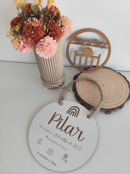 Placa redonda branca em madeira com texto Pilar, vaso com flores e decoração em madeira