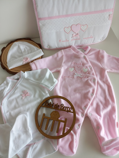 Conjunto de roupas de bebé em rosa e branco com bordados, chapéu, e placa decorativa em madeira