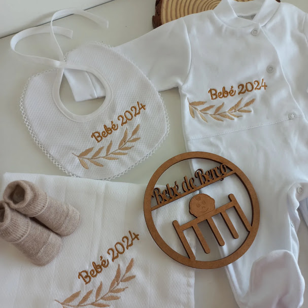 Conjunto de roupa e acessórios brancos para bebé com bordados castanhos 'Bebé 2024' e decoração de madeira