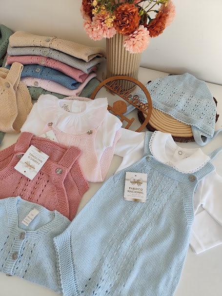 Roupas de bebé em malha azul e cor-de-rosa com golas brancas, boné azul e flores secas