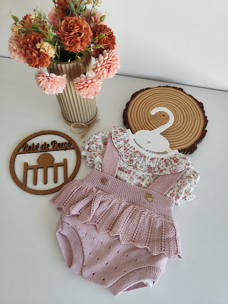 Roupa de bebé floral com saia rosa, vaso com flores e objetos decorativos em madeira