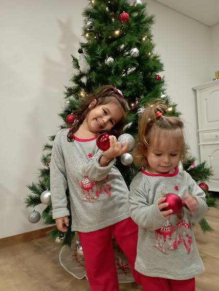 Crianças com pijamas cinza e vermelhos em frente a árvore de Natal decorada com bolas
