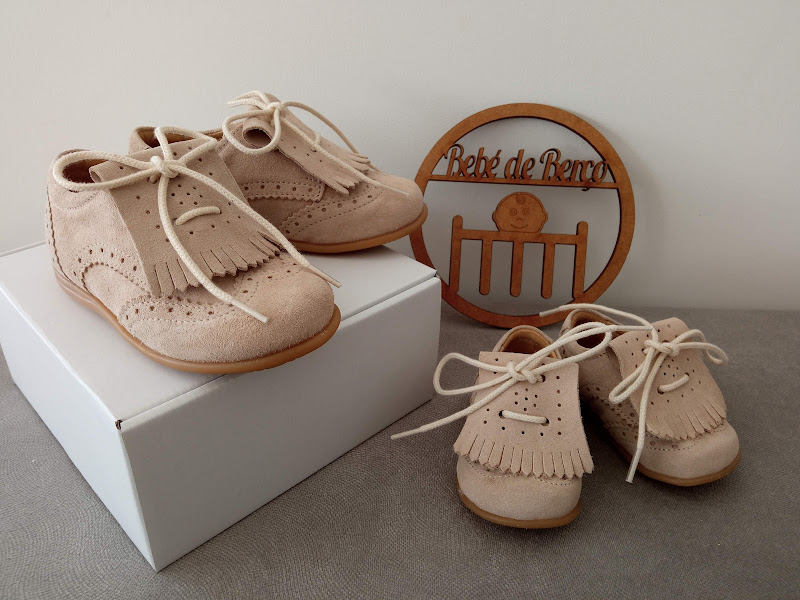 Sapatos de bebé bege em camurça com franjas e placa de madeira com texto