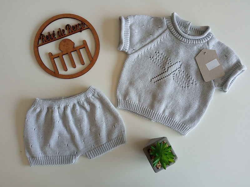 Conjunto de roupa de bebé cinzenta clara em malha com padrão de laço e calções, círculo decorativo de madeira e planta pequena