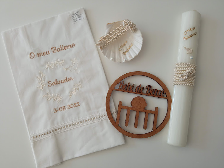 Conjunto de batismo com toalha branca bordada, vela, concha e decoração em madeira.