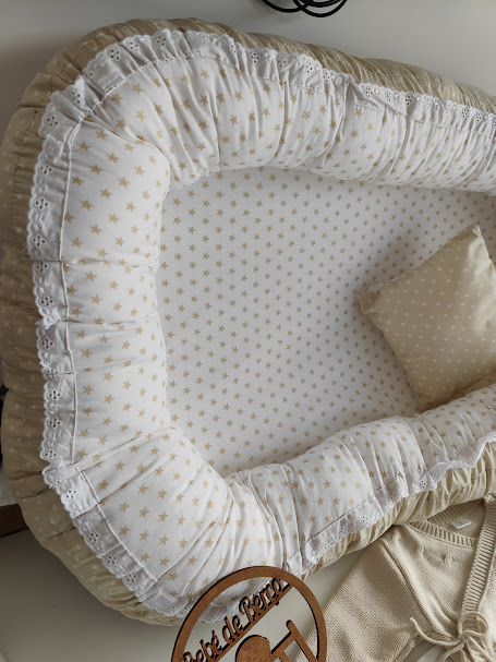 Cama para bebé com padrão de estrelas douradas e almofada bege com estrelas brancas