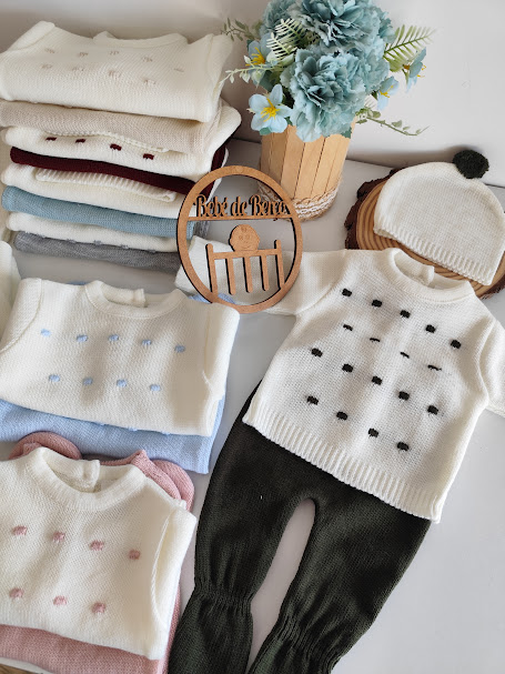 Conjunto de roupa de bebé com camisolas de malha e calças, placa de madeira Bebé de Reyes e vaso com flores
