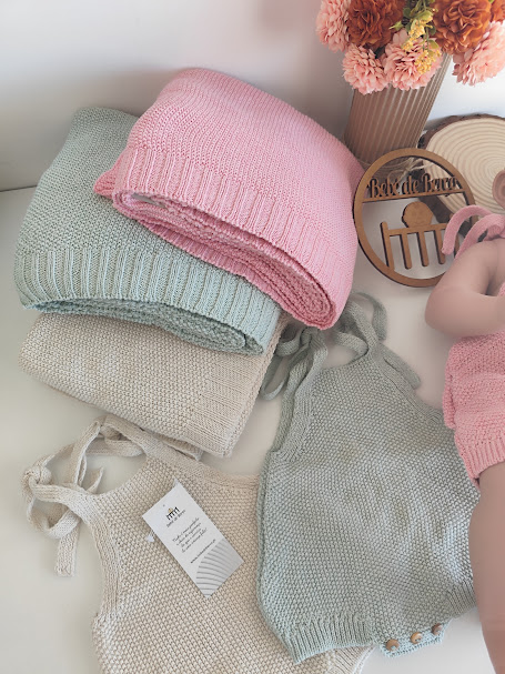 Roupas de bebé em malha verde-claro, rosa e bege, com boneco e flores