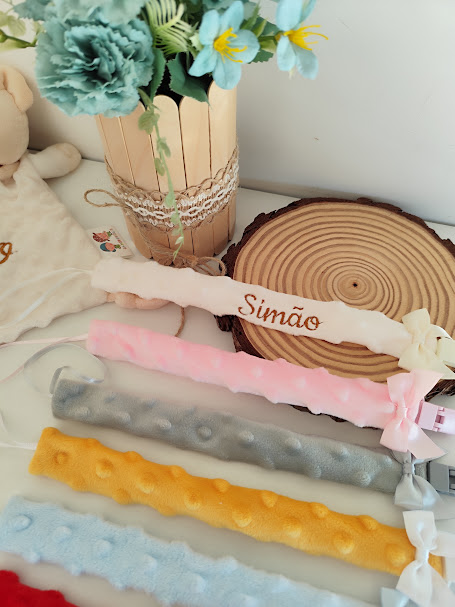 Porta-chupetas coloridos com texturas e nome Simão, vaso com flores azuis e base que imita madeira