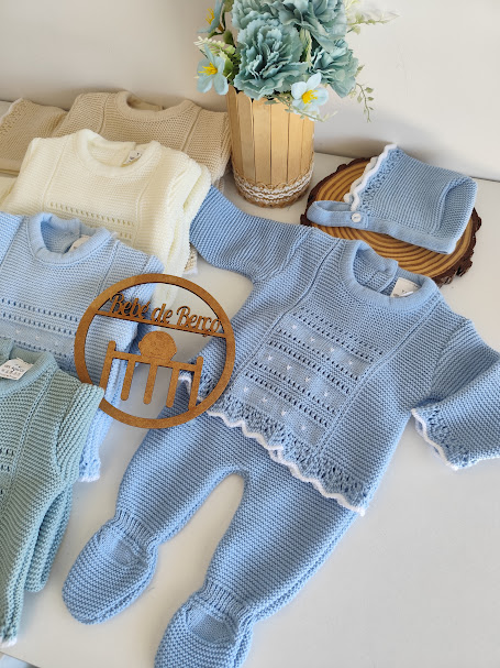 Conjunto de roupa de bebé em malha tricô azul claro, branco e bege com touca, placa de madeira e flores em vaso