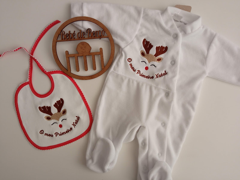 Conjunto de bebé com babete e pijama brancos com rena e texto, e ornamento redondo de madeira