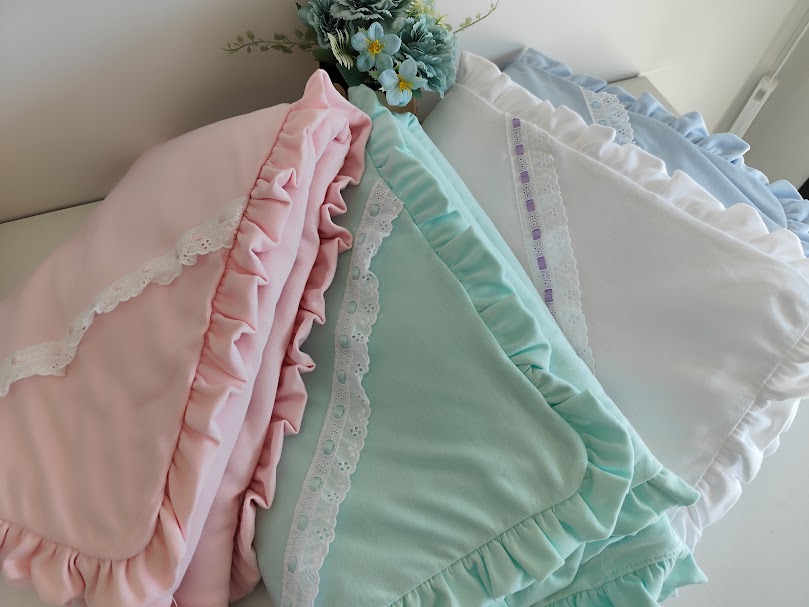 Três mantas com babados em rosa, verde água e branco junto a um arranjo floral azul