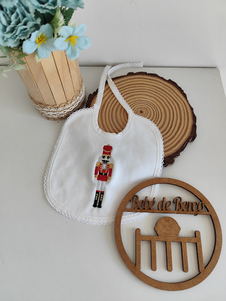 Babete branco com bordado colorido de soldadinho da rainha, decoração em madeira e flor numa jarra