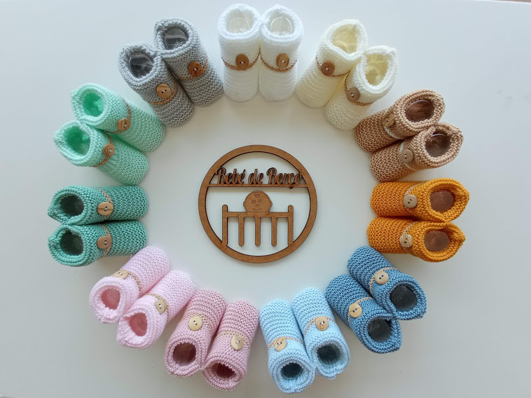 Vários pares de sapatinhos de bebé tecidos em croché coloridos organizados em círculo com texto central