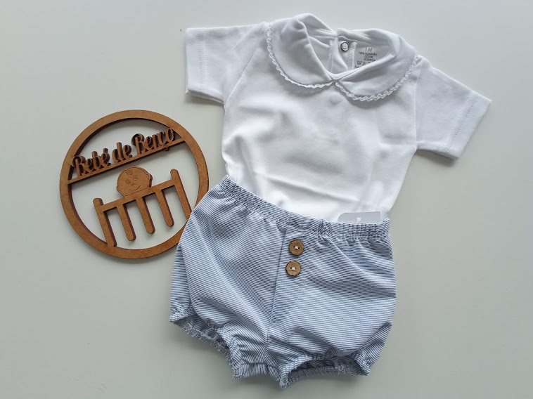 Conjunto de roupa para bebé com t-shirt branca e calções azuis às riscas, perto de placa de madeira com texto