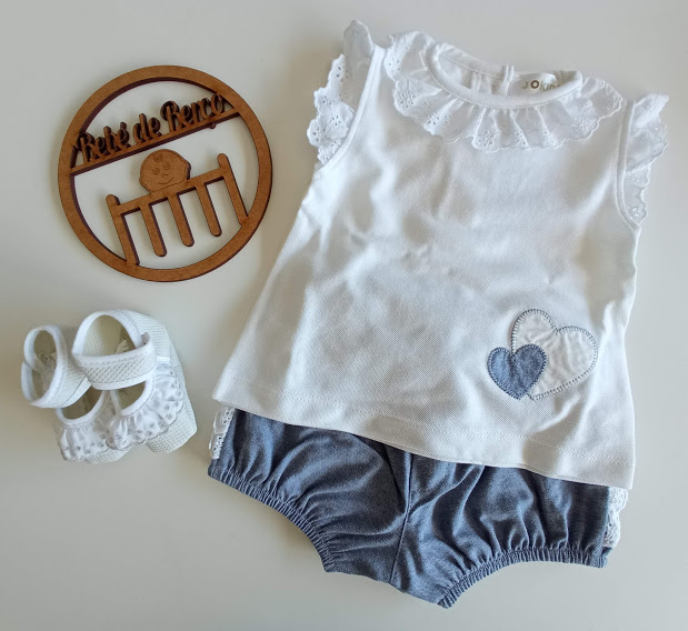 Conjunto de roupa de bebé com top branco, calções azuis e sapatinhos brancos, decorado com ícone de madeira