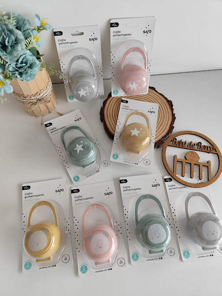 Capas porta-chupetas coloridas em embalagens sobre mesa com flores e decoração de madeira