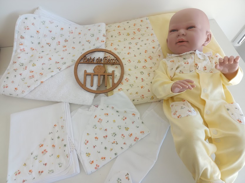 Conjunto de roupa e acessórios para bebé em algodão com padrões florais e um boneco de bebé vestido de amarelo