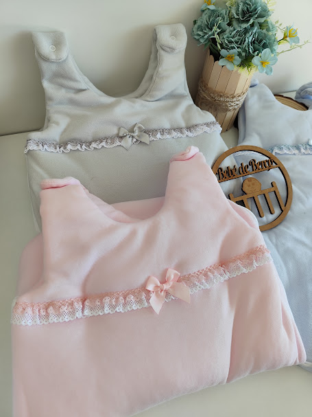 roupinhas de bebé em veludo rosa, bege e cinza com flores artificiais e placa de madeira