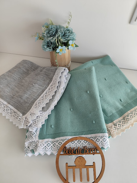 Mantinhas de bebé verdes e cinzentas com renda, flores azuis e suporte decorativo em madeira