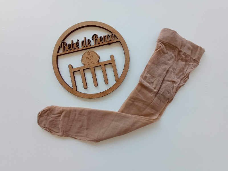 Meia-calça bege clara e placa decorativa de madeira com texto 'Petite de Paris'