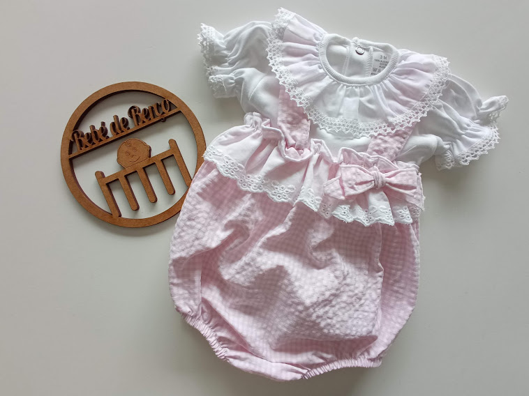 Body infantil rosa e branco com renda e laço, decoração de madeira redonda ao lado