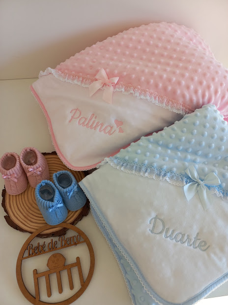 Mantinhos de bebé rosa e azul claro, com sapatinhos combinando e sinal de madeira com texto Bebé de Franco.