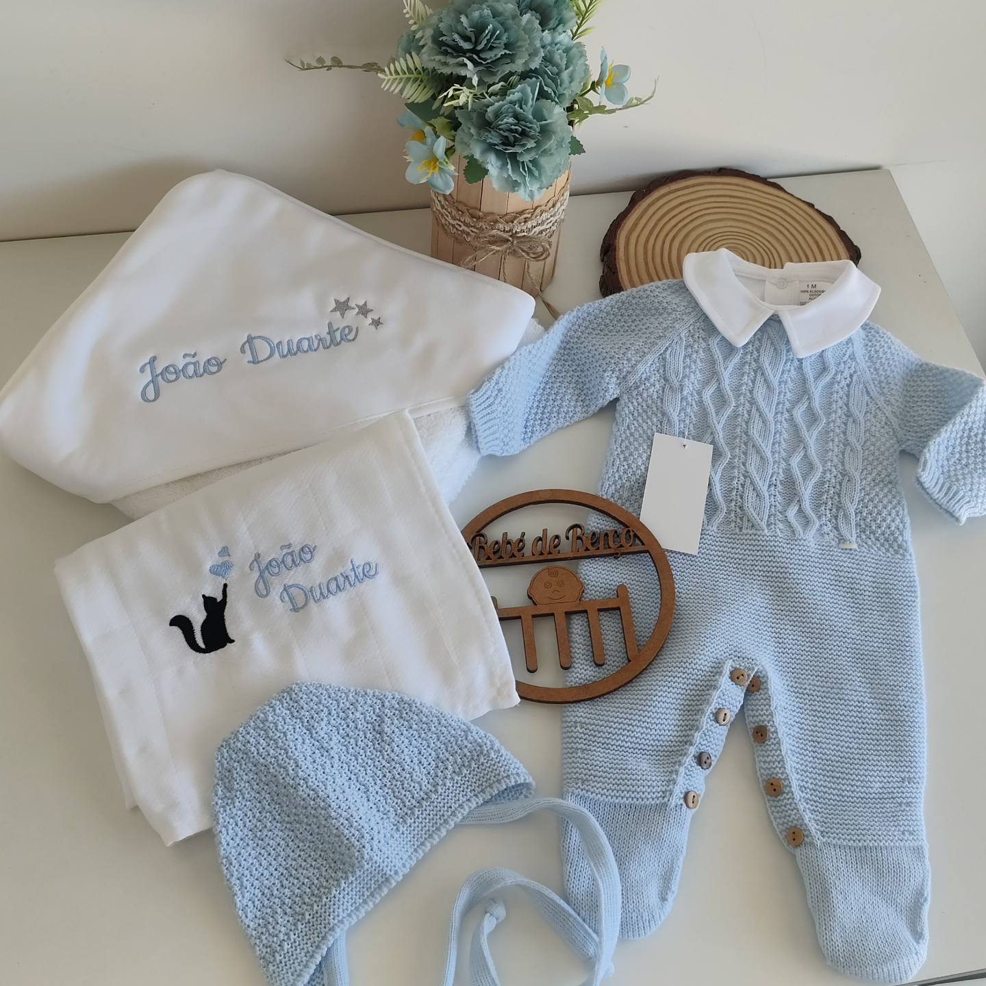 Conjunto de roupa de bebé azul com fraldas brancas bordadas e vaso de flores