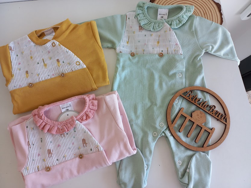 Três macacões de bebé coloridos com padrões e placa de madeira com texto