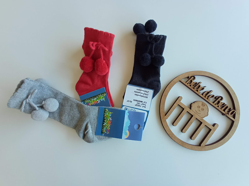 Três pares de meias com pompons e uma placa de madeira com texto