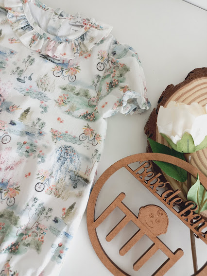 Body de bebé branco com padrão de bicicletas e flores ao lado de decoração em madeira