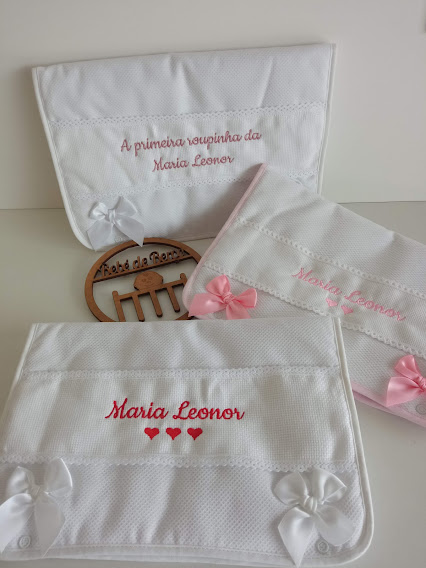 Três toalhas brancas bordadas com nomes e laços em cetim em superfície clara