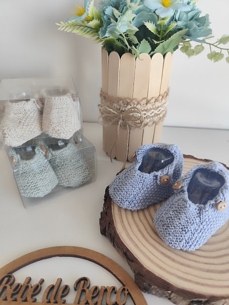Chinelos de bebê em lã azul com botões, base de madeira e chinelos em caixas transparentes