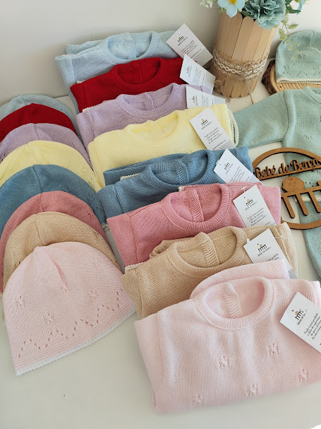 Conjunto colorido de camisolas e gorros de malha expostos com etiquetas e decoração floral.