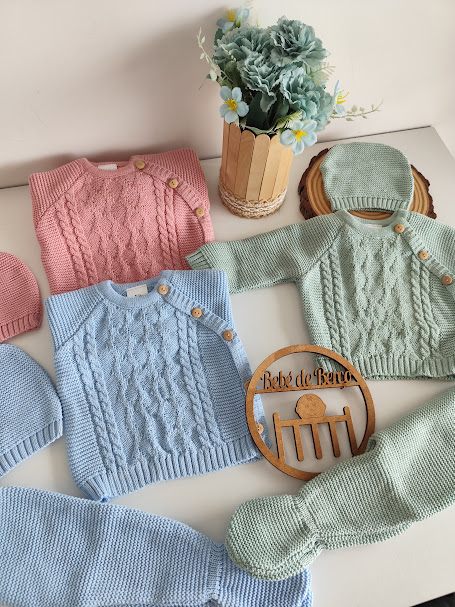 Roupas de bebé em tricô coloridas com botões, vaso de flores e placa de madeira Bebé de Berço
