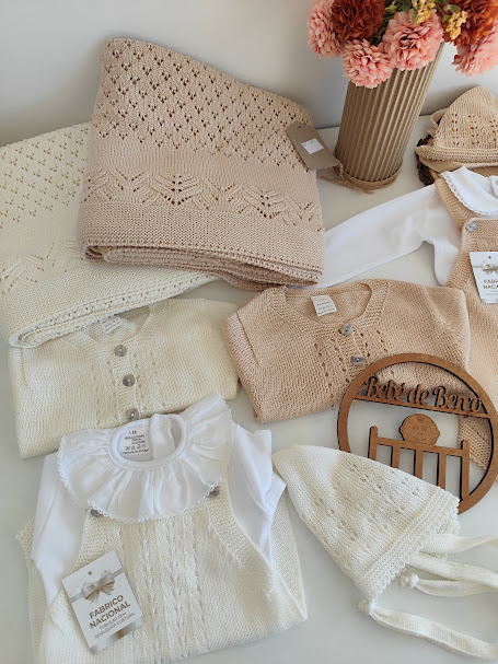 Roupa e acessórios de malha para bebé em tons creme e bege com etiquetas e ornamento de madeira