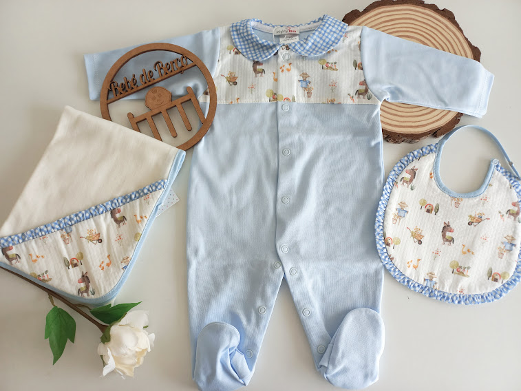 Conjunto de roupa de bebé azul e creme com macacão, babete e manta, decorado com padrão de animais, sobre fundo branco com elementos em madeira