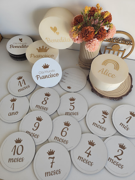 Placas redondas e ovaladas de madeira com gravações com números e nomes, e vaso com flores secas