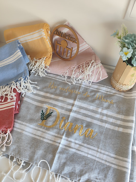 Toalhas de tecido coloridas com franjas e toalha cinza com texto dourado e planta em vaso